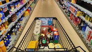 Ein Einkaufswagen wird durch einen Gang im Supermarkt geschoben. © IMAGO / blickwinkel 