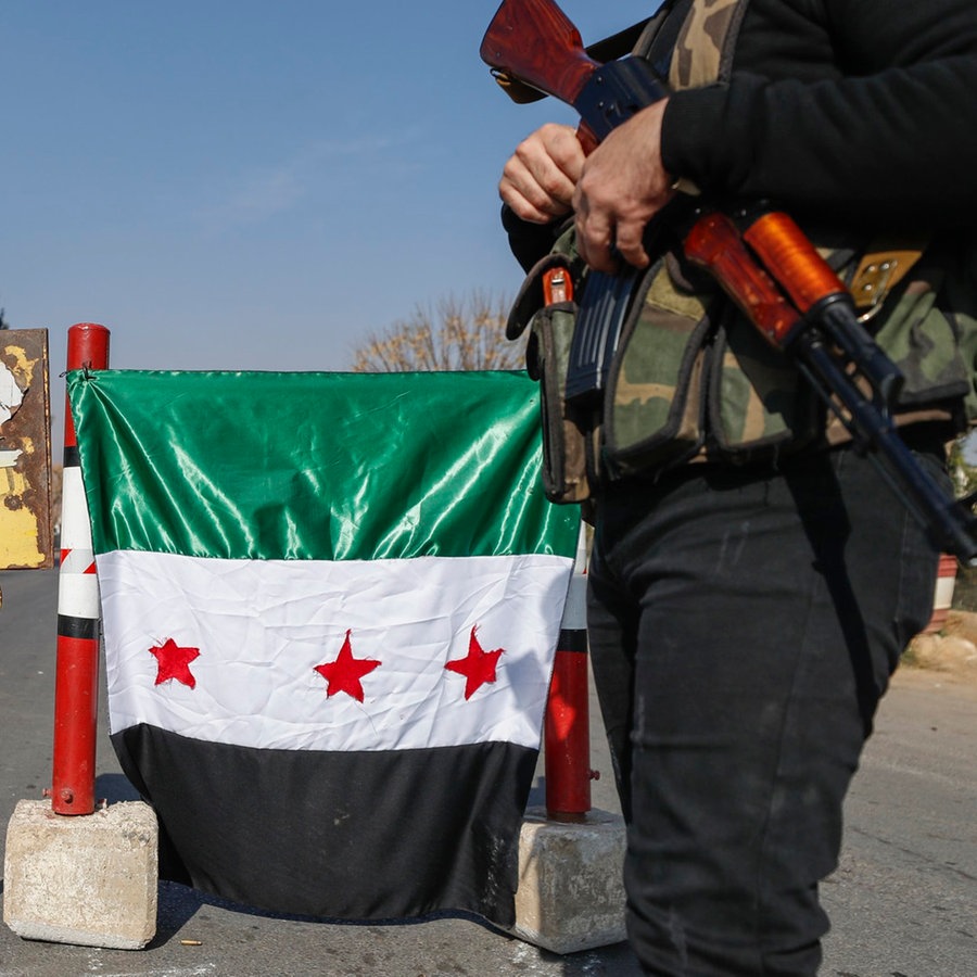 Ein syrischer Oppositionskämpfer steht sschwer bewaffnet an einem beflaggten Kontrollpunkt in Damaskus. © AP Foto: Omar Sanadiki