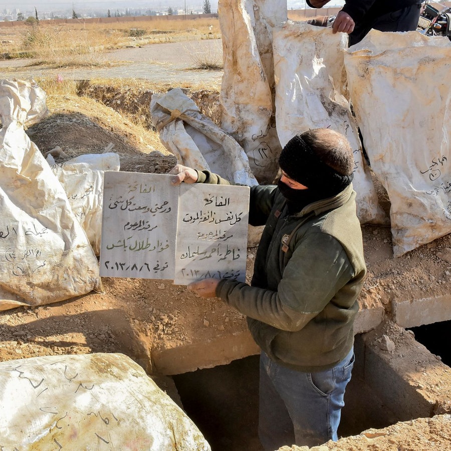Ein Arbeiter hält ein Schild mit Informationen über den Inhalt eines Massengrabs im Bereich der Bagdad-Brücke außerhalb von Damaskus, Syrien. © picture alliance / Middle East Images | Fadel Itani Foto: Fadel Itani