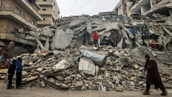 Menschen betrachten die Trümmer eines zerstörten Wohnhauses im syrischen Idlib. © dpa bildfunk Foto: Anas Alkharboutli