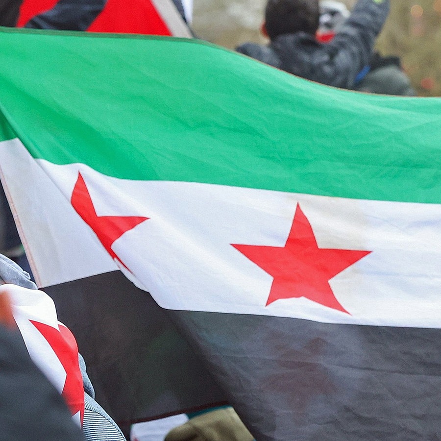Menschen feiern mit Fahnen bei einer Kundgebung den Sturz des syrischen Assad-Regimes. © dpa bildfunk Foto: Bodo Marks