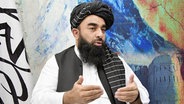 Taliban-Sprecher Zabihullah Mujahid spricht in einem Interview vor einer bunten Wand. © picture alliance / Kyodo 