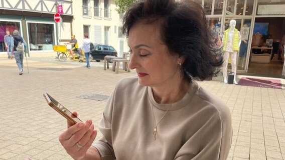 Tanja Koktash schaut auf ihr Handy und lächelt bei der Erinnerung an die Fotoaufnahmen. © NDR/Lydia Callies Foto: Lydia Callies