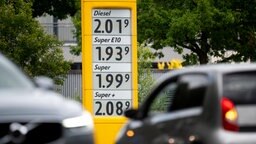 Die Preise für Kraftstoffe sind auf der Anzeige einer Tankstelle zu sehen, davor fahren Autos vorbei. © Daniel Reinhardt/dpa 
