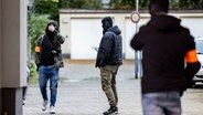 Drei Polizeibeamte stehen nach der Festnahme des Verdächtigen am Dienstagnachmittag auf dem Garagenhof des Hauses, in dem der Mann festgenommen wurde. © dpa Foto: Christoph Reichwein