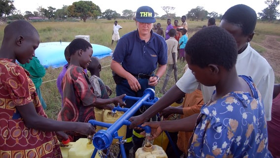 THW-Mitarbeiter und Kinder an einer Trinkwasseranlage. © THW 