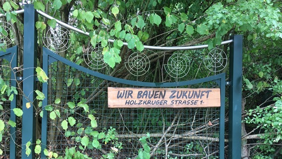 Ein Holzschild am Zaun des Projektes "Wir bauen Zukunft" mit gleichnamiger Aufschrift. © NDR Foto: Marc Hoffmann