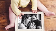 Ein Baby hält ein schwarz-weißes Familienfoto im Rahmen in den Händen © Colourbox Foto: #232319