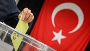 Ein Wähler wirft seinen Wahlumschlag in eine Urne in einem Wahllokal für die türkische Präsidentschaftswahl in der Messe Hannover. © dpa Foto: Julian Stratenschulte