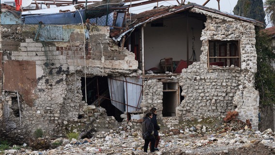 Menschen gehen im Februar 2024 in der Altstadt von Antakya (Türkei) an zerstörten Häusern vorbei. © Boris Roessler/dpa 