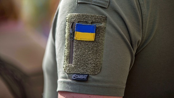 Eine ukrainische Flagge ist auf den T-Shirt-Ärmel eines Soldaten aufgenäht. © IMAGO / ZUMA Wire 