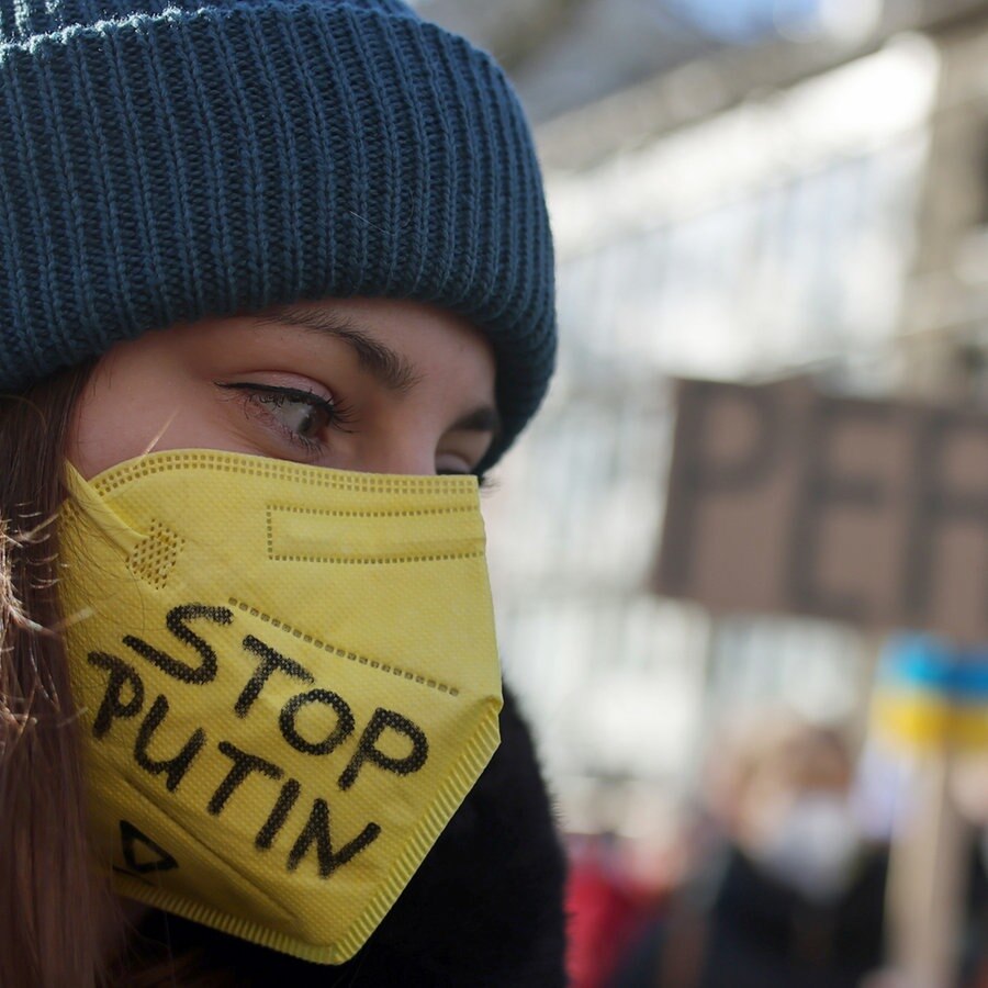 Eine Teilnehmerin der Friedensdemonstration am Rosenmontag trägt eine gelbe FFP2-Maske mit der Aufschrift "Stop Putin". © picture alliance/dpa | Oliver Berg Foto: Oliver Berg