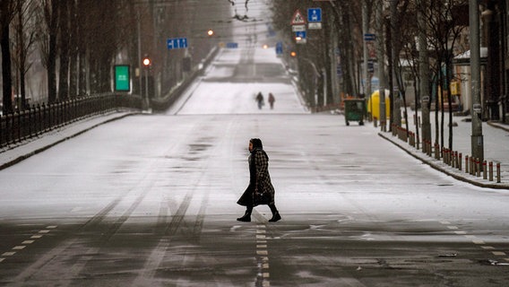 Eine Frau überquert im Halbdunklen eine leere Straße in Kiew in der Ukraine. © dpa picture alliance/AP Foto: Emilio Morenatti