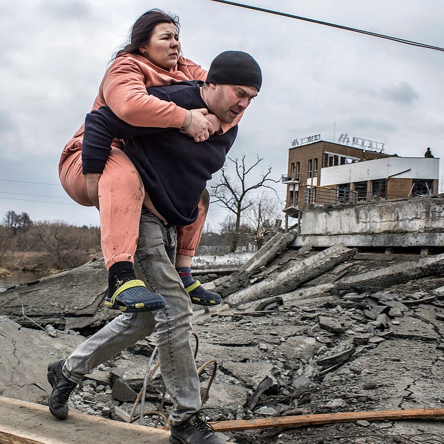 Ein Mann trägt eine Frau, als sie auf der Flucht aus der Stadt Irpin einen improvisierten Weg zwischen Trümmern überqueren. © AP/dpa Foto: Oleksandr Ratushniak