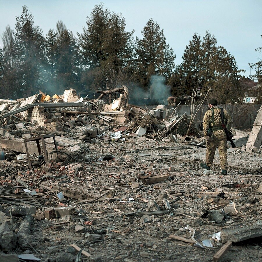 Ein Freiwilliger der ukrainischen Territorialen Verteidigungskräfte geht durch die Trümmer einer durch einen russischen Bombenangriff zerstörten Autowaschanlage. © dpa picture alliance/AP Foto: Felipe Dana