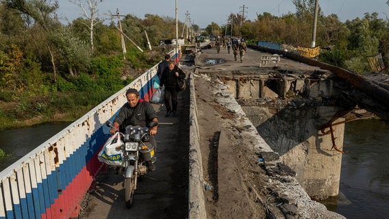 Kupjansk: Ein Mann fährt mit seinem Motorrad auf einer zerstörten Brücke über den Fluss Oskil © Evgeniy Maloletka/AP/dpa 
