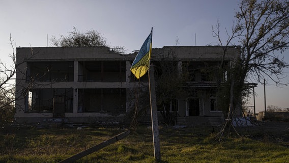 Eine ukrainische Flagge vor einem beschädigten Gebäude im Raum Cherson. © picture alliance / AA Foto: Metin Aktas