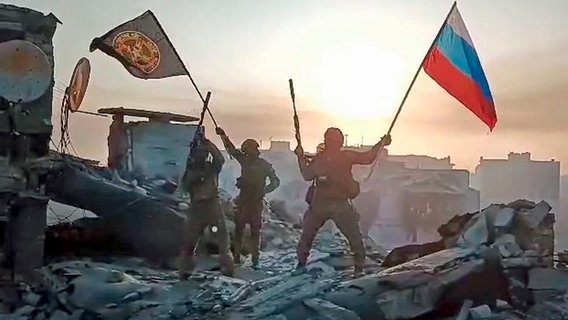 Ein Video-Standbild soll zeigen, wie Soldaten eine russische National- und eine Wagner-Flagge auf einem beschädigten Gebäude in der ukrainischen Stadt Bachmut schwenken. © dpa picture alliance / Zoonar Foto: Leonid Altman