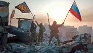 Ein Video-Standbild soll zeigen, wie Soldaten eine russische National- und eine Wagner-Flagge auf einem beschädigten Gebäude in der ukrainischen Stadt Bachmut schwenken. © dpa picture alliance / Zoonar Foto: Leonid Altman
