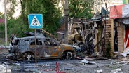 Ein von einer russischen Rakete zerstörtes Auto steht qualmend vor den Trümmern eines Hauses. © picture alliance / Anadolu | Kherson Regional Military Administration of Ukraine / Handout 