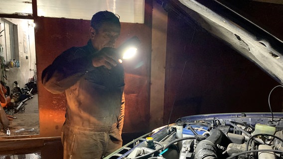 Mit einer Taschenlampe leuchtet Automechaniker Ivan auf den Motor eines Autos. © ARD Foto: Andrea Beer