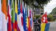 Ein Mann platziert die Flagge der Schweiz während der letzten Vorbereitungen für den Ukraine-Friedensgipfel. © picture alliance/dpa/KEYSTONE/EDA/POOL | Foto:  Urs Flueeler