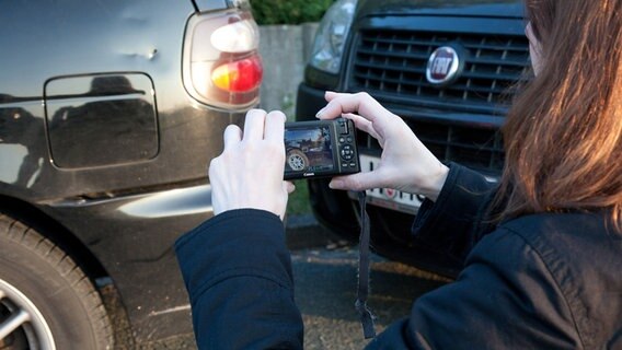 Eine Frau fotografiert einen Unfallschaden an einem Auto. © picture alliance/ dpa Themendienst Foto: Kai Remmers