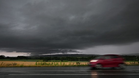 Ein Auto fährt über eine Landstraße, während am Horizont eine Unwetterfront aufzieht. © dpa bildfunk Foto: Julian Stratenschulte