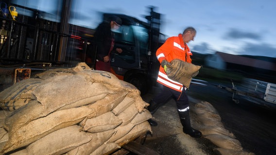 Ein Mann mit Feuerwehrweste holt einen Sandsack von einer Palette voller weiterer Sandsäcke. © dpa-Bildfunk Foto: Julian Stratenschulte