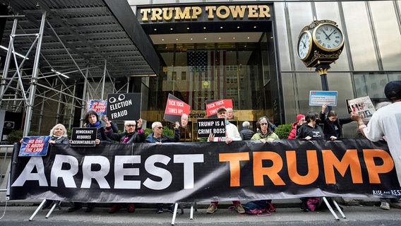 Demonstranten stehen mit einem Banner mit der Aufschrift "Trump verhaften" vor dem Trump Tower in New York. © dpa bildfunk/AP Foto: Bryan Woolston