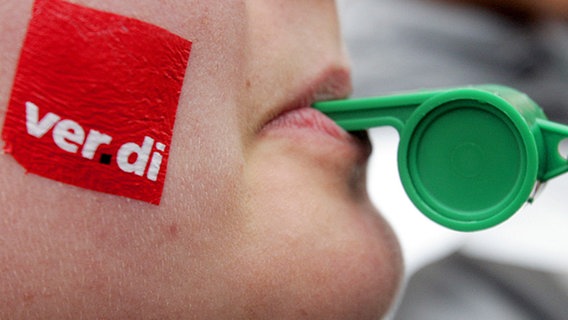 Frau mit ver.di-Logo auf der Wange und Trillerpfeife im Mund. © dpa Foto: Frank May