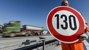 Ein Straßenwärter hält an der Autobahn A81 am Hegaublick ein Schild mit der Aufschrift "130" in den Händen. © picture alliance Foto: Patrick Seeger