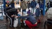 Menschen füllen ihre Wasserflaschen auf. Die Bewohner der ukrainischen Hauptstadt griffen auf der Suche nach Wasser zu leeren Flaschen und drängten sich in Cafes, um Strom zu erhalten und sich aufzuwärmen. © picture alliance/dpa/AP | Evgeniy Maloletka Foto: | Evgeniy Maloletka