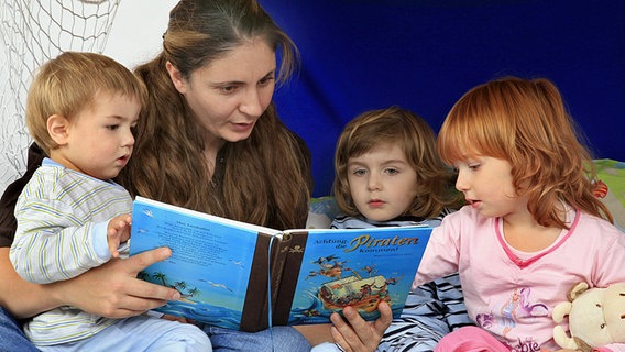 Eine Mutter liest ihren drei Kindern aus einem Buch vor. © dpa picture alliance Foto: fotototo