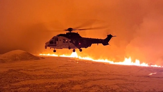 Ein Hubschrauber fliegt in der Nähe von Magma, das auf einem Hügel in der Nähe von Grindavik auf der isländischen Halbinsel Reykjanes fließt. © dpa-Bildfunk 