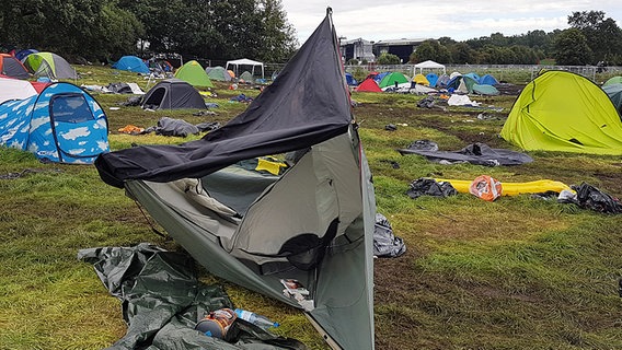 Ein kaputtes Zelt im Vordergrund, umgeben von weiteren Zelten im Hintergrund, steht auf einer Wiese. © NDR Foto: Oliver Kring