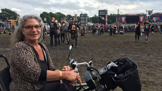 Eine Frau im Rollstuhl vor dem Festivalpanorama des Wacken Openairs © NDR Foto: Schenk, Niklas