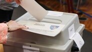Eine Person wirft einen Wahlzettel in eine Urne in Thüringen. © Bodo Schackow/dpa 