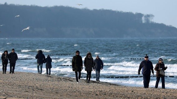 Spaziergänger sind am Ostseestrand von Warnemünde (Mecklenburg-Vorpommern) unterwegs, der leicht bewölkte Himmel lässt bei eher herbstlichen Temperaturen immer wieder mal die Sonne durch. © dpa bildfunk Foto: Bernd Wüstneck