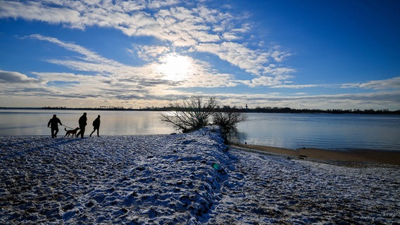 Menschen sind bei sonnigem Winterwetter am schneebedeckten Elbstrand des Falkensteiner Ufers bei Hamburg-Blankenese unterwegs. © dpa-Bildfunk Foto: Christian Charisius