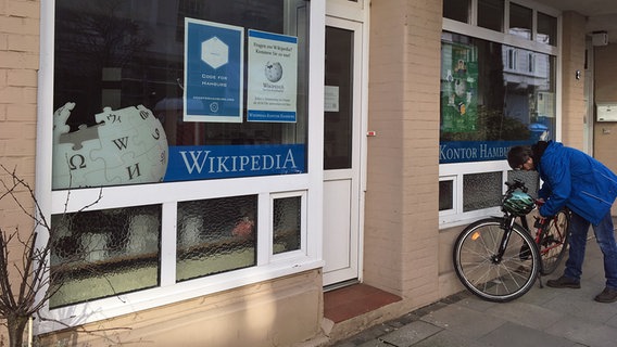 Die Fensterscheibe eines kleinen Büros in einem Gebäude ist von außen zu sehen. An dem Fenster hängen Plakate und Schriftzüge von Wikipedia. Die Fensterscheibe eines kleinen Büros in einem Gebäude ist von außen zu sehen. An dem Fenster hängen Plakate und Schriftzüge von Wikipedia. © NDR Foto: Marc Hoffmann