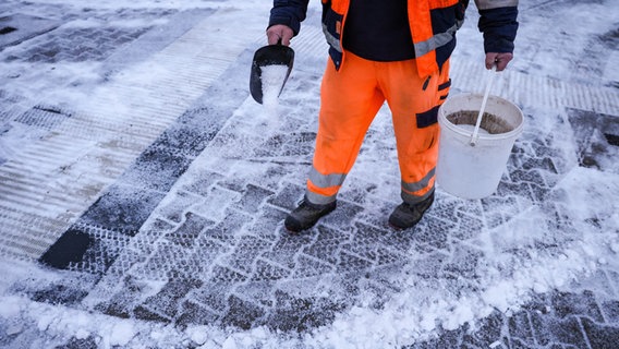 Ein Mitarbeiter des Winterdienstes verteilt Streusalz bei Regen und Schneeglätte auf den Fußweg an einer Straßenkreuzung. © picture alliance/dpa Foto: Jan Woitas