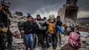 Zivilisten und Mitglieder des syrischen Zivilschutzes führen Such- und Rettungsmaßnahmesuchen in den Trümmern eines zerstörten Gebäudes in Harem durch. © Anas Alkharboutli/dpa 