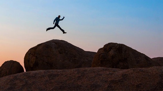 Ein Mann springt auf Felsen. © imago stock & people Foto: imagebroker