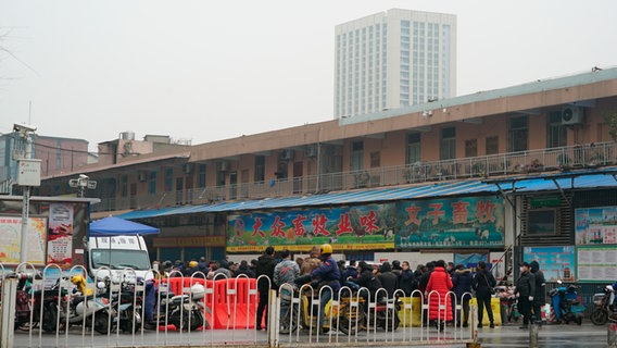 Vor dem geschlossenen Huanan Wholesale Seafood Market im chinesischen Wuhan versammeln sich Menschen. Der Markt wurde wegen eines Corona-Ausbruchs Anfang 2020 geschlossen. (Foto vom 21. Januar 2020) © picture alliance / ASSOCIATED PRESS | Dake Kang 