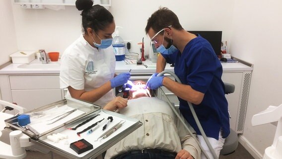 Eine Zahnärztin und ein angehender Zahnarzthelfer behandeln einen Patienten. © NDR Info Foto: Bettina Less