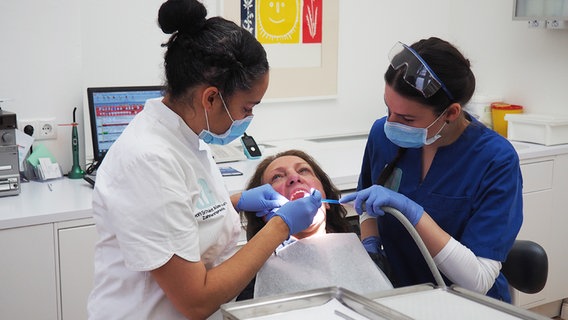 Eine Zahnärztin und eine angehende Zahnarthelferin behandeln eine Patientin. © NDR Info Foto: Bettina Less