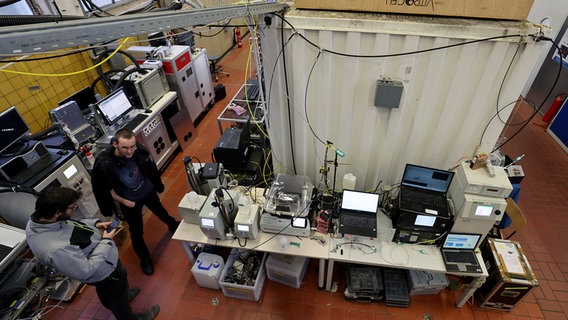 Rostock: In der Forschungshalle der Fakultät für Maschinenbau und Schiffstechnik der Universität steht ein Mobiles Biologisches Labor (r), das aus München kam, neben anderen Test- und Laborgeräten. © Bernd Wüstneck/dpa +++ dpa-Bildfunk +++ Foto: Bernd Wüstneck/dpa +++ dpa-Bildfunk +++