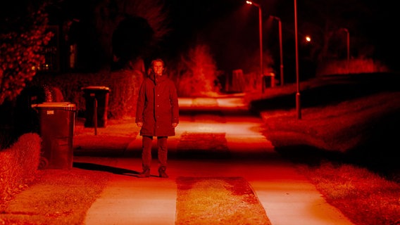 Ein Mann steht in Ahrenshoop in einer Straße, die rot ausgeleuchtet ist. © dpa-Bildfunk Foto: dpa-Bildfunk