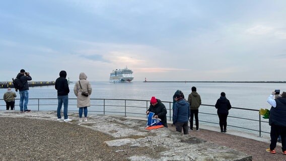Menschen beobachten vom Ufer aus das Kreuzfahrtschiff AIDAdiva, das  in den Rostocker Hafen einfährt. © NDR Foto: Jürn-Jakob Gericke